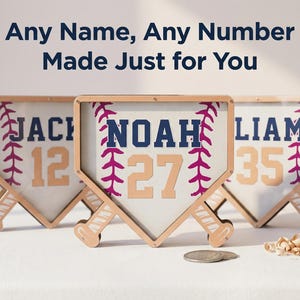 Puede incluir: Tres placas con nombres con tem&aacute;tica de b&eacute;isbol con nombres y n&uacute;meros personalizados. Cada placa tiene la forma de un plato de home, con un marco de madera y un dise&ntilde;o de puntada de b&eacute;isbol. El texto "Any Name, Any Number Made Just for You" est&aacute; en la parte superior.