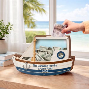 Può includere: Un salvadanaio in legno a forma di barca con una vela bianca e dettagli blu. Il salvadanaio è pieno di banconote, e una mano sta inserendo una banconota da 100 euro. Il testo sul salvadanaio recita "The Johnson Family Cruise Fund 2026."