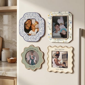 May include: Four decorative picture frames with family photos. The frames have various shapes and colors, including blue, green, and cream. Text on the frames includes "I love you, Daddy!", "Happy Father's Day", and "Best Dad Ever".