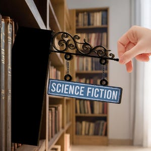 May include: A black metal bookshelf divider with an ornate scroll design and a blue sign that reads "SCIENCE FICTION." The sign hangs from chains. The background shows a library filled with books.