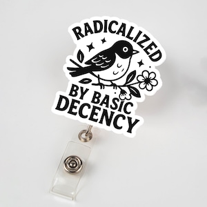 May include: A white badge reel with a black and white graphic of a bird perched on a branch with a flower. The text on the badge reel reads "RADICALIZED BY BASIC DECENCY". The badge reel has a clear plastic strap and a metal clip.