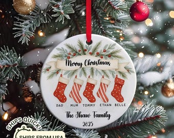 May include: A round Christmas ornament with a red ribbon, featuring a festive design. The ornament displays the text "Merry Christmas" above five red stockings. Below, it reads "The Thaw Family 2025" with family member names.