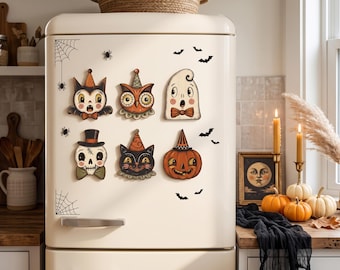May include: A set of six Halloween-themed magnets featuring a cat, owl, ghost, skull, black cat, and pumpkin, all wearing party hats or bow ties. The magnets are displayed on a cream-colored refrigerator decorated with black spiderweb and bat decals.