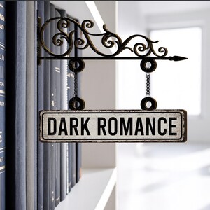 May include: A decorative metal sign with the words "DARK ROMANCE" in black lettering. The sign is suspended by chains from an ornate, scrolled bracket. The background features a bookshelf with dark blue books.