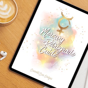 May include: A digital tablet displays a "Mercury Retrograde Guide" with a watercolor background of pastel colors and gold accents. The text is in a script font. A cup of coffee and earbuds are on the wooden surface.