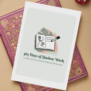 Puede incluir: Una portada de diario blanca con un diseño de hoja verde y un pequeño libro abierto con un bolígrafo. El texto en la portada dice "365 Days of Shadow Work A Guided Journal for Emotional Healing and Self Discovery."