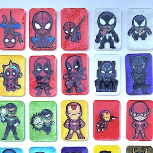 May include: A collection of rectangular, colorful superhero-themed magnets. Each magnet features a different character, including Spider-Man, Batman, and Captain America. The magnets are arranged in a grid pattern, with a variety of colors and designs.