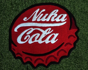 May include: A red, black, and white Nuka Cola bottle cap rug. The rug is circular with the words "Nuka Cola" in white script. The rug is on a green surface.