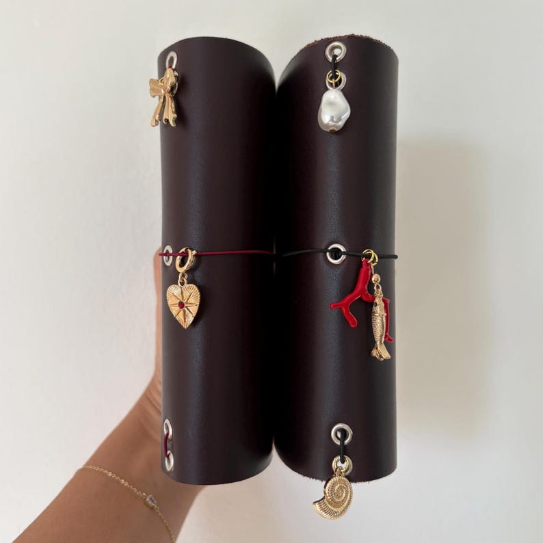 May include: Two dark brown leather journal covers with decorative gold charms. Charms include a bow, a pearl, a heart, a coral branch, a fish, and a seashell. The journals are held together with elastic bands.