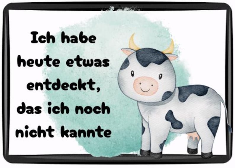 May include: A framed print featuring a watercolor illustration of a cartoon cow with black spots and yellow horns. The text reads "Ich habe heute etwas entdeckt, das ich noch nicht kannte."