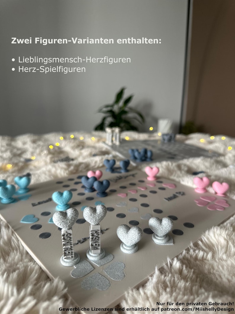 May include: A board game with heart-shaped game pieces in blue, pink, and gray. The game board is light gray with scattered heart and dot decorations. Text on the board reads "Zwei Figuren-Varianten enthalten: Lieblingsmensch-Herzfiguren, Herz-Spielfiguren."