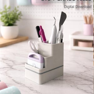 Puede incluir: Un organizador de herramientas gris con múltiples compartimentos, que contiene varias herramientas de manualidades como tijeras, bolígrafos y una espátula. El texto "tool holder STL + BAMBU FILES Digital Download" es visible. El organizador está sobre una superficie de mármol.