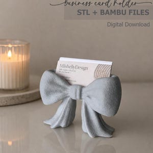 Peut inclure: Un porte-cartes de visite gris clair imprimé en 3D en forme de nœud. Le support contient une carte de visite blanche avec le texte MiishellyDesign. L'image inclut le texte business card holder STL + BAMBU FILES Digital Download.