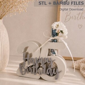 May include: A white, three-dimensional '25' birthday gift holder with the words 'Happy Birthday' in silver script. A small vase with white flowers is attached to the top. The words 'birthday gift' and 'Digital Download' are also visible.