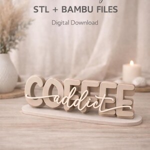 May include: A digital download featuring a custom design for 3D printing. The text reads "COFFEE" in large, beige, block letters with the word "addict" in a white, cursive script layered over the front, all mounted on a flat, oval base.