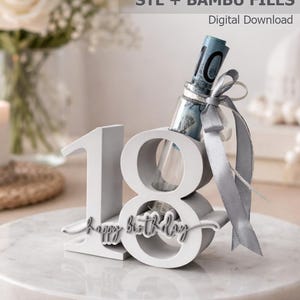 May include: A white 3D-printed number 18 stand with the text "happy birthday" in cursive script. A clear glass tube is inserted into the number eight, containing a rolled-up banknote tied with a silver ribbon. Text reads "birthday gift STL + BAMBU FILES Digital Download" and "personal use only."
