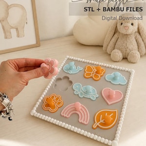 May include: A square gray shape puzzle board with a white beaded border featuring various pastel-colored inserts including a whale, butterfly, cloud, turtle, heart, paw print, rainbow, and leaf. Text reads shape puzzle STL + BAMBU FILES Digital Download.