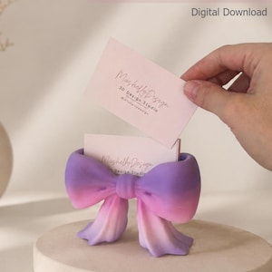 Puede incluir: Un tarjetero impreso en 3D con forma de lazo y acabado en degradado morado y rosa. El soporte contiene tarjetas de visita de color rosa claro con el texto Mushelly Design 3D Design Studio. El texto dice business card holder STL + BAMBU FILES.
