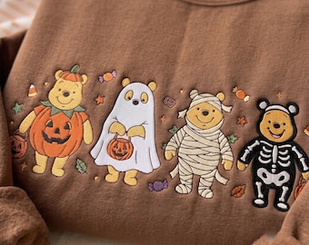 Puede incluir: Una sudadera marrón de cuello redondo con un diseño bordado de cuatro personajes de Winnie the Pooh disfrazados de Halloween: calabaza, fantasma, momia y esqueleto, rodeados de pequeños dulces y hojas de otoño bordadas.