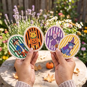 May include: Four oval-shaped coasters with scalloped edges featuring Winnie the Pooh characters in Halloween costumes: Tigger as a pirate, Pooh in a pumpkin suit, Piglet as a bat, and Eeyore as a wizard, each set against a striped background.