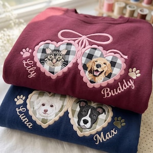 May include: A maroon sweatshirt featuring two embroidered hearts with black and white buffalo plaid backgrounds, showcasing a cat and a dog, with the names Lily and Buddy. Below, a navy sweatshirt displays two hearts with pet portraits and names.