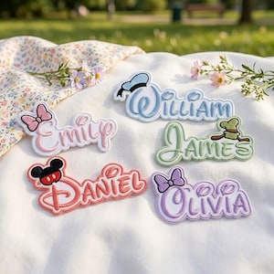 May include: Five embroidered name patches featuring Disney-inspired motifs. The patches display the names Emily in pink with a bow, William in blue with a sailor hat, James in green with a hat, Daniel in red with mouse ears, and Olivia in purple with a bow.