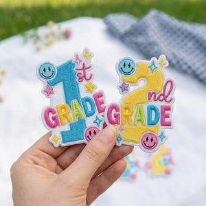 May include: Two embroidered patches featuring the text 1st GRADE and 2nd GRADE. The 1st GRADE patch is blue with pink and yellow accents, while the 2nd GRADE patch is yellow with pink and blue accents. Both include smiley faces and stars.
