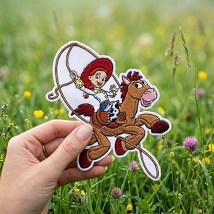 May include: An embroidered patch featuring a cartoon cowgirl with red hair and a white shirt riding a brown horse. The cowgirl is holding a lasso above her head. The patch has a white border and depicts the characters in vibrant colors.