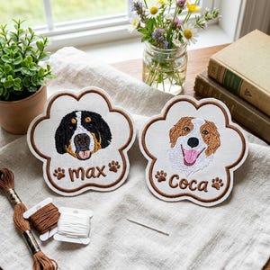 May include: Two paw-shaped fabric patches featuring embroidered dog portraits. The left patch shows a black, white, and brown dog with the name Max embroidered below. The right patch shows a brown and white dog with the name Coca embroidered below.