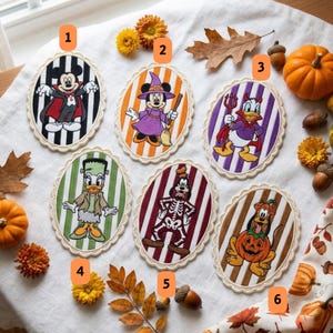 Könnte beinhalten: Sechs ovale gestickte Aufnäher mit Disney-Figuren in Halloween-Kostümen: Mickey als Vampir, Minnie als Hexe, Donald als Teufel, Daisy als Frankensteins Monster, Goofy im Skelettkostüm und Pluto in einem Kürbis.