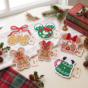 May include: Six decorative Christmas ornaments featuring gingerbread-style designs, including a bell cluster, a wreath, a gingerbread person, a bow-adorned figure, a gingerbread house, and a tree, each paired with a numbered tag from one to six.