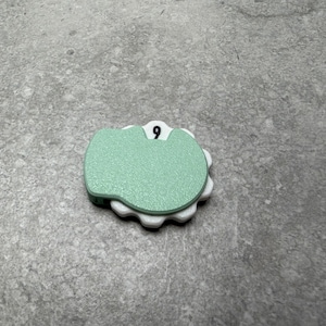 May include: A mint green and white decorative object with the number 9 on top. The object has a rounded shape with a scalloped edge. The number 9 is in a black font.