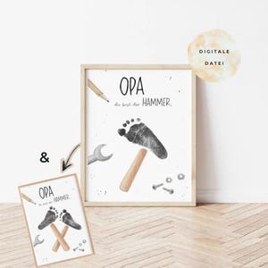 Op de afbeelding: Een ingelijste print met het woord "OPA" en de zin "du bist der HAMMER" in het Duits. De print toont een voetafdrukontwerp dat op een hamer lijkt, met gereedschap zoals een moersleutel en schroeven. Een kleinere print met hetzelfde ontwerp is ook zichtbaar.