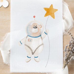 Könnte beinhalten: Aquarellillustration eines Bären-Astronauten, der einen goldenen Stern hält. Der Bär trägt einen weißen Raumanzug mit blauen Akzenten und einen transparenten Helm. Eine rote Antenne sitzt oben. Das Bild hat eine skurrile, kindliche Qualität.