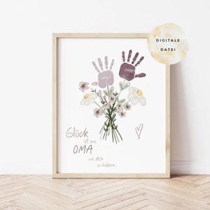 Op de afbeelding: Ingelijste print met een boeket bloemen en handafdrukken in paarse en bruine tinten. De print bevat Duitse tekst en een hartsymbool. De lijst is van licht hout. De Duitse tekst luidt "Glück ist eine OMA wie dich zu haben".
