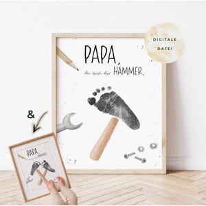 Op de afbeelding: Een ingelijste print met de tekst "PAPA, du bist der HAMMER." heeft een hamerontwerp met voetafdruk, een potlood, een moersleutel en hardware. Een kleinere ingelijste print met een vergelijkbaar ontwerp is ook zichtbaar.