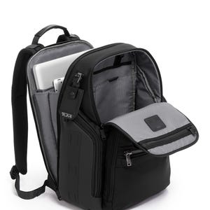 May include: Black backpack with multiple compartments, including a laptop sleeve. The backpack has a top handle, adjustable shoulder straps, and a front zippered pocket. A tag with the brand name "TUMI" is attached. The interior is gray.