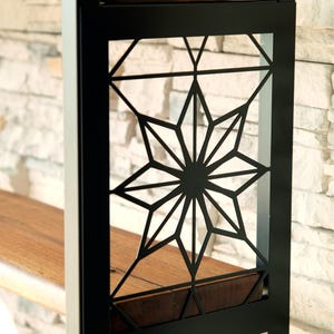 Puede incluir: Estanter&iacute;a de metal negro con un dise&ntilde;o geom&eacute;trico de estrella. La estanter&iacute;a tiene una superficie de madera y est&aacute; colocada contra una pared de piedra de color claro. El dise&ntilde;o de estrella es una caracter&iacute;stica destacada.