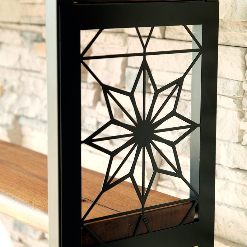 Puede incluir: Estanter&iacute;a de metal negro con un dise&ntilde;o geom&eacute;trico de estrella. La estanter&iacute;a tiene una superficie de madera y est&aacute; colocada contra una pared de piedra de color claro. El dise&ntilde;o de estrella es una caracter&iacute;stica destacada.