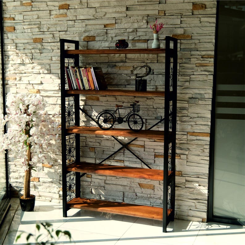 Puede incluir: Una estanter&iacute;a alta de madera con estructura de metal negro y detalles decorativos. Los estantes est&aacute;n llenos de libros y objetos decorativos, incluyendo una bicicleta en miniatura. La estanter&iacute;a est&aacute; contra una pared de piedra.