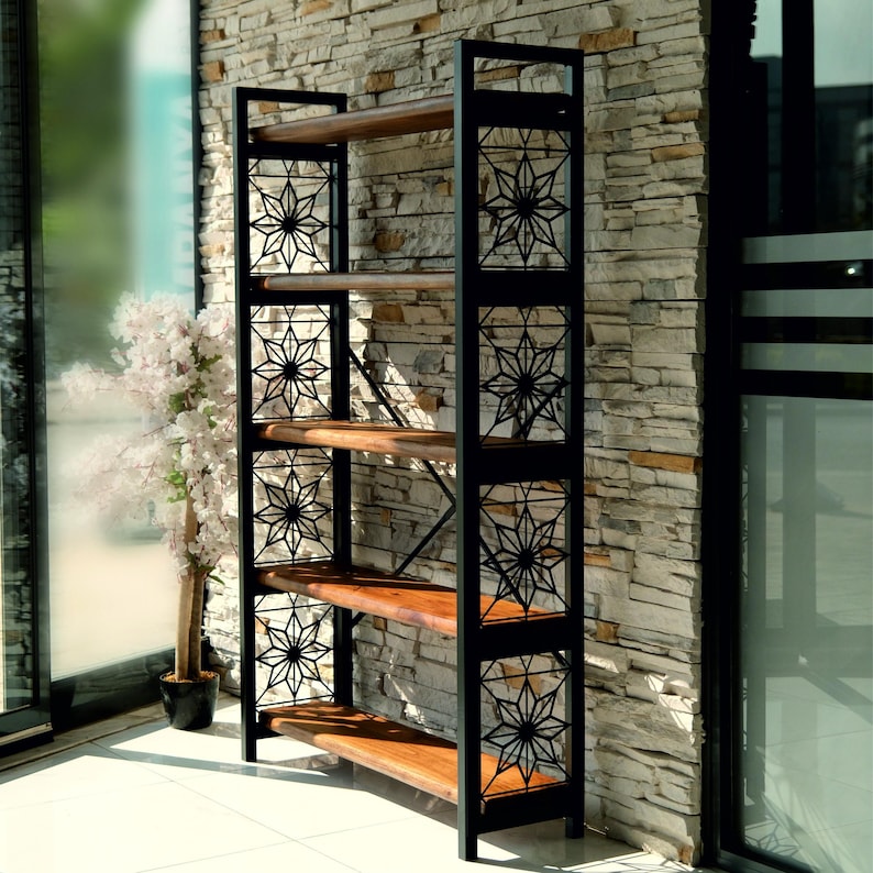 Puede incluir: Estanter&iacute;a alta de metal negro con cinco estantes de madera. Los laterales presentan dise&ntilde;os decorativos de estrellas. La estanter&iacute;a est&aacute; colocada contra una pared de piedra y junto a una ventana, mostrando un dise&ntilde;o moderno e industrial.