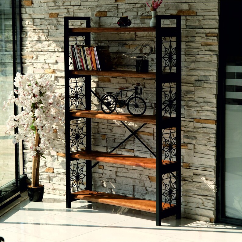 Puede incluir: Estanter&iacute;a alta con estructura de metal negro y estantes de madera. El marco presenta cortes en forma de estrella. Los estantes exhiben libros y adornos, incluyendo una bicicleta en miniatura. Un &aacute;rbol de flores blancas est&aacute; a la izquierda.