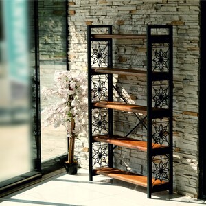 Puede incluir: Una estanter&iacute;a alta de marco abierto con cuatro estantes de madera. El marco de metal negro presenta recortes decorativos en forma de estrella. Los estantes son de madera natural. La estanter&iacute;a se coloca contra una pared de piedra, con un &aacute;rbol en maceta visible en el fondo.