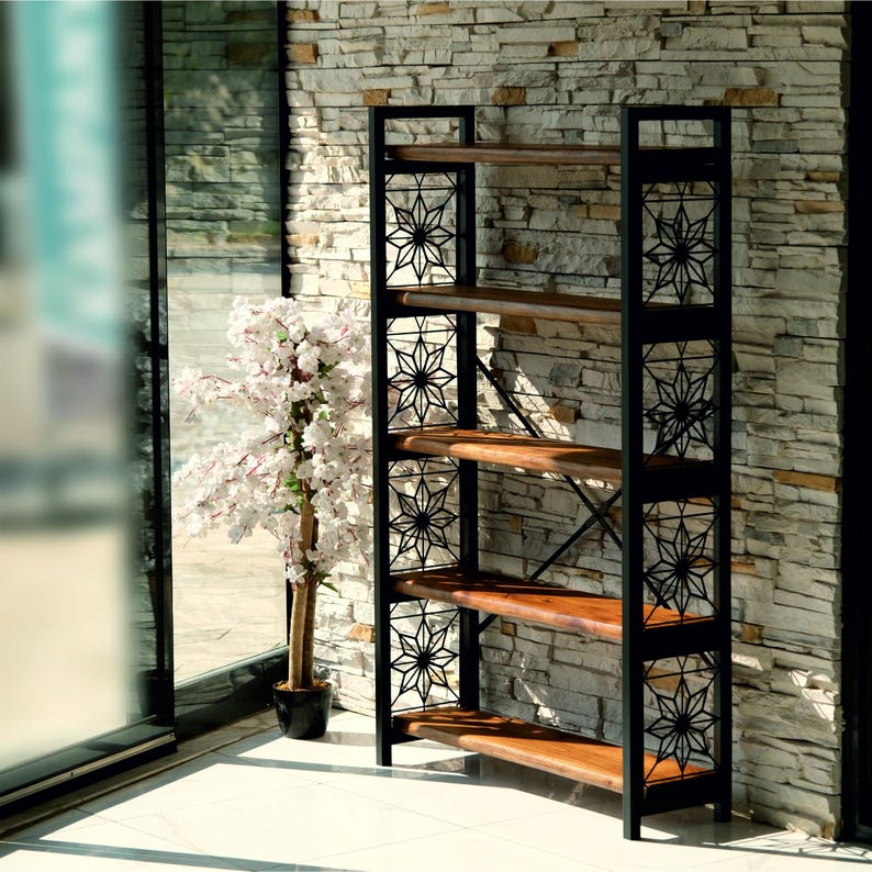 Puede incluir: Una estanter&iacute;a alta de marco abierto con cuatro estantes de madera. El marco de metal negro presenta recortes decorativos en forma de estrella. Los estantes son de madera natural. La estanter&iacute;a se coloca contra una pared de piedra, con un &aacute;rbol en maceta visible en el fondo.