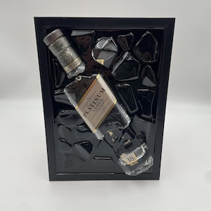 Op de afbeelding: Een zwart omlijst kunstwerk met drie gedeeltelijk zichtbare whiskyflessen. De flessen zijn voorzien van de labels "Johnnie Walker Platinum Label" en "18". De achtergrond is een zwarte textuur.