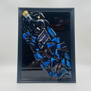 Op de afbeelding: Een ingelijst kunstwerk met een geconstrueerde fles Johnnie Walker Blue Label. Het kunstwerk bestaat uit gefragmenteerde stukken van de fles, met blauwe en zwarte tinten en het label "Blue Label". De lijst is zwart.