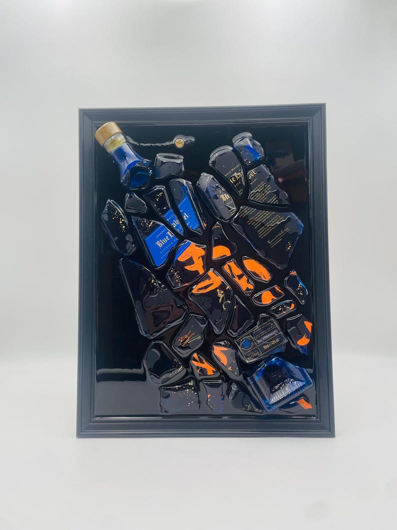 May include: Abstract art piece featuring fragments of blue and black liquor bottles with orange accents, set against a black background within a dark gray frame. The artwork showcases a unique, modern design.