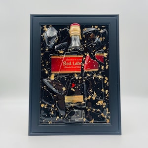 K&ouml;nnte beinhalten: Gerahmtes Kunstwerk mit einer Johnnie Walker Red Label Flasche. Die Flasche ist in schwarzem Harz mit Goldblatt-Akzenten und klaren Harzsplittern eingebettet. Der Rahmen ist dunkelblau.