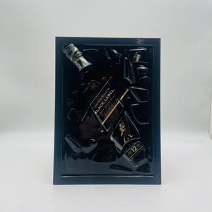 May include: A framed artwork featuring a Johnnie Walker Black Label whiskey bottle and fragments. The black frame surrounds a dark background with the bottle and pieces of glass. The label is visible, and the number 12 is displayed.