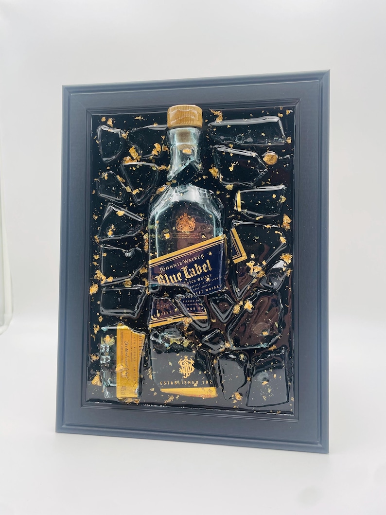 May include: Framed artwork featuring a Johnnie Walker Blue Label whiskey bottle. The bottle is set against a black background with gold leaf accents and encased in a dark blue frame. The label reads "Blue Label" and "Johnnie Walker".